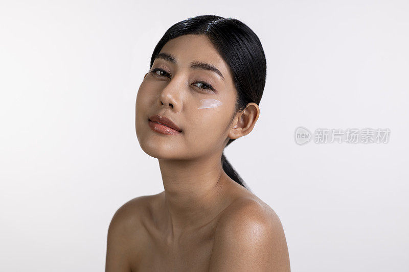 迷人的年轻亚洲女性正在脸上涂抹保湿霜