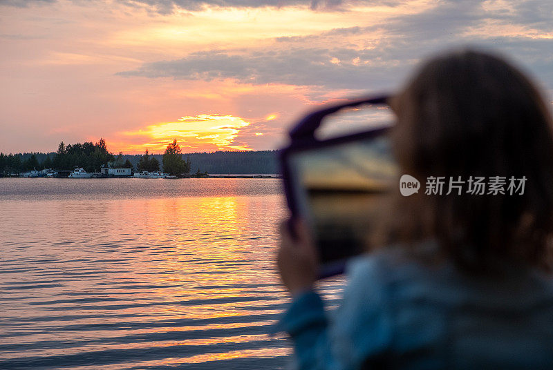 一个女孩，一个8岁的孩子，在湖上看日落，并在平板电脑上拍照。