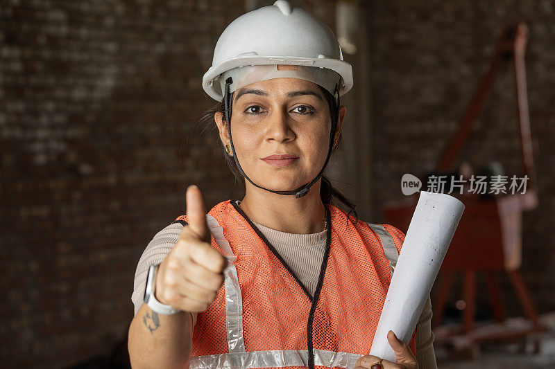 拿着蓝图的女工程师在工地竖起大拇指