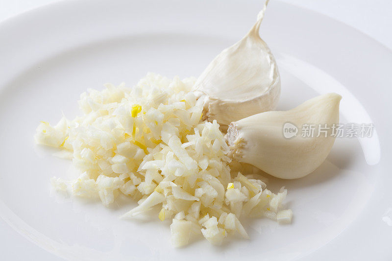 两瓣大蒜和切碎的大蒜放在一个白色盘子上，特写