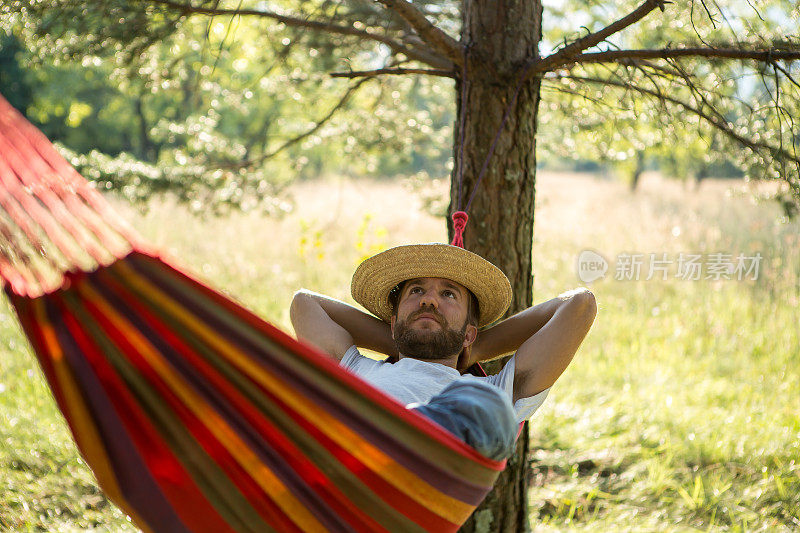 年轻男子戴着草帽，躺在彩色吊床上