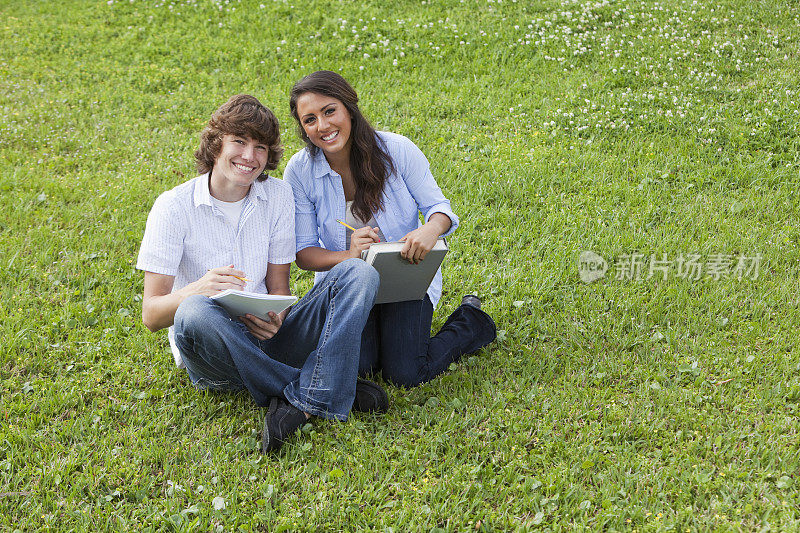 一对青少年情侣坐在草地上学习