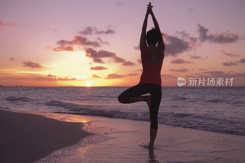 一个女人的剪影瑜伽姿势在日落在海滩上