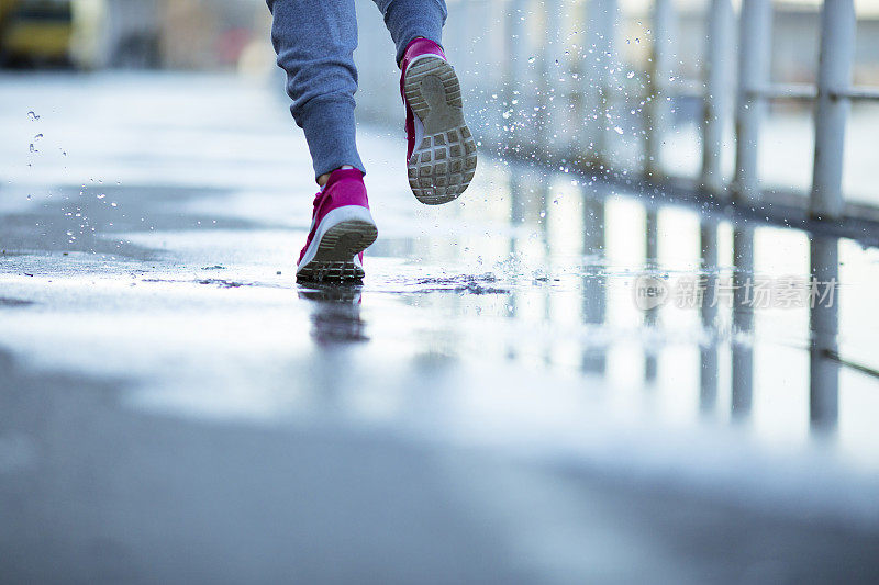 年轻女性在雨天在沥青操场上跑步