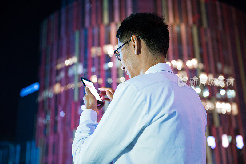 商人在现代城市的夜晚使用他的智能手机