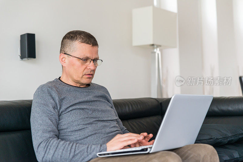 一个老人坐在沙发上用笔记本电脑