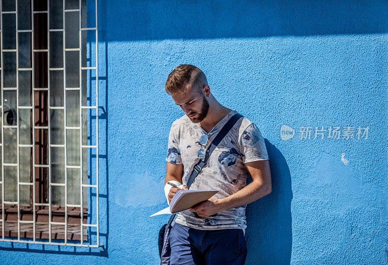 一个年轻人靠着墙站着看书