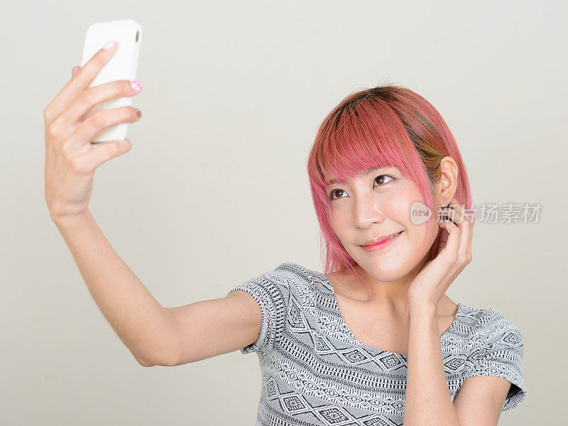 工作室拍摄的年轻美丽的亚洲女子用手机在白色背景下做视频博客