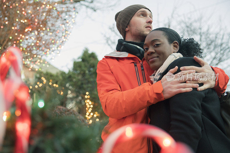 在纽约布鲁克林寒冷的冬日里，美丽的黑人年轻女子和英俊的年轻男子拥抱在一起，一起看圣诞彩灯，尽情欢乐。