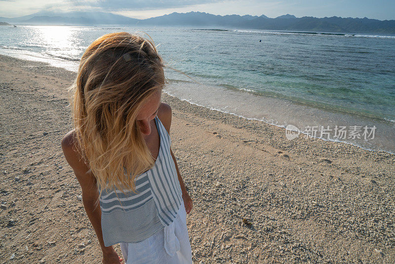 年轻女子走在热带海滩在日出在巴厘岛享受在热带气候的目的地海滩假日-人们旅行度假海滩概念