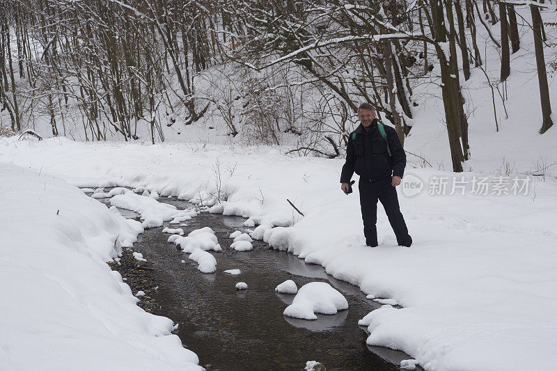 快乐的成年人徒步旅行在下雪的冬天大自然旁边流动的小溪在森林里