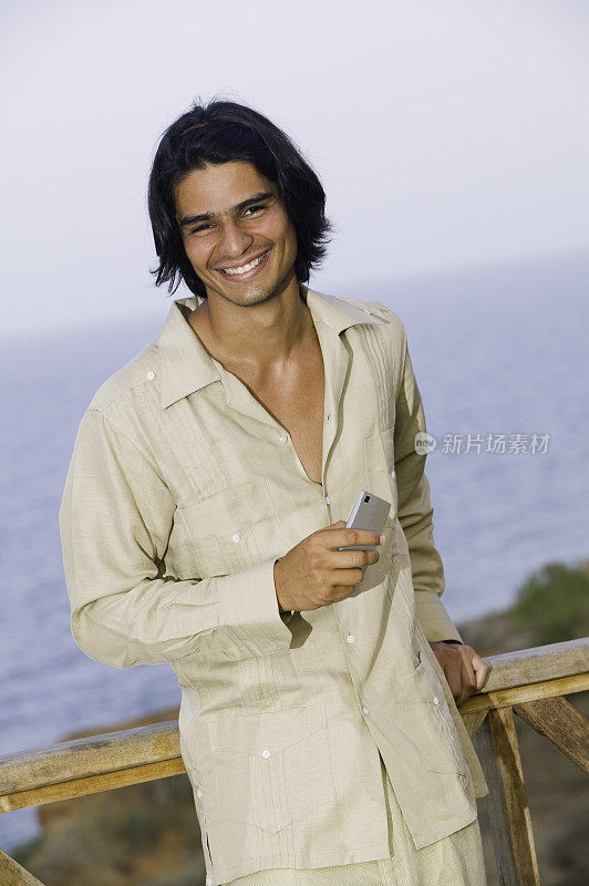 一名男子穿着瓜亚贝拉衬衫在海边的户外露台上，手里拿着手机