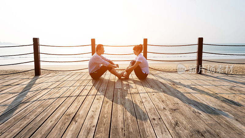 一对夫妇坐在海边的木板路上