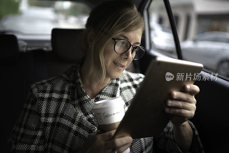 女商人在出租车里工作，用着平板电脑，喝着咖啡