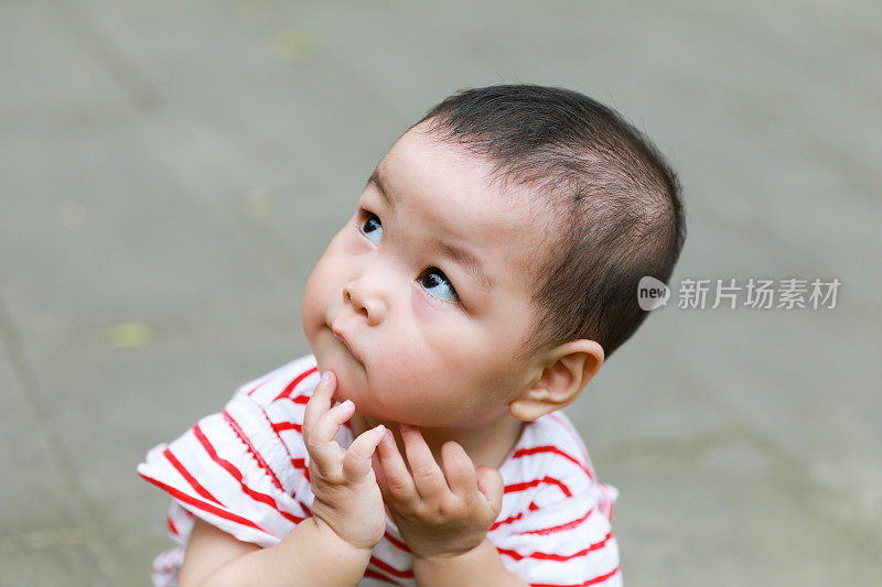 一个中国小女孩蹲伏在地上，双手托着下巴的特写