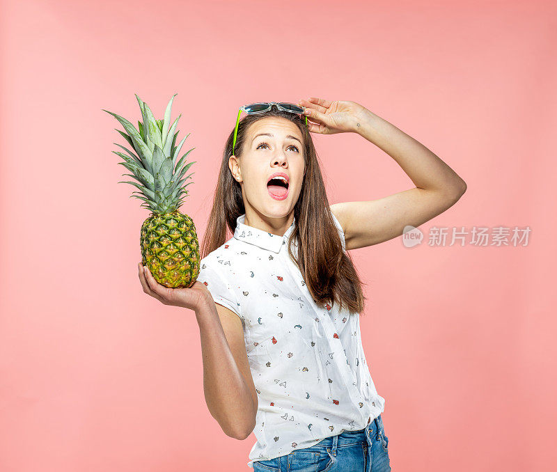 年轻女子拿着菠萝和抬头与嘴张开在珊瑚背景