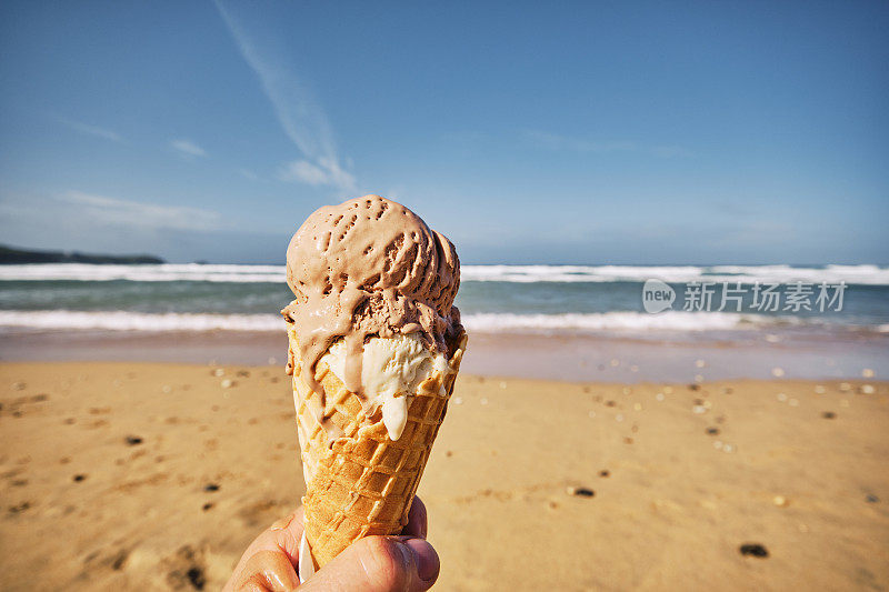 在一个阳光明媚的秋天，在纽基，康沃尔的Fistral海滩，POV手握一个巧克力和香草冰淇淋蛋筒。