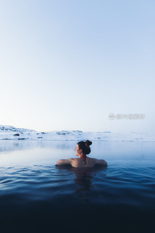 一名女子正在温泉池中沐浴，可以看到冰岛的雪山和冰湖