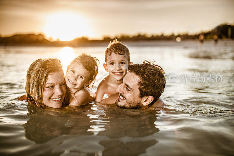 快乐的父母和他们的孩子们在日落时在海上放松。
