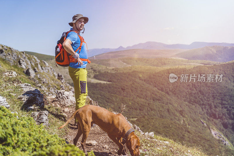 年轻的男性徒步旅行者背包和他的狗看风景