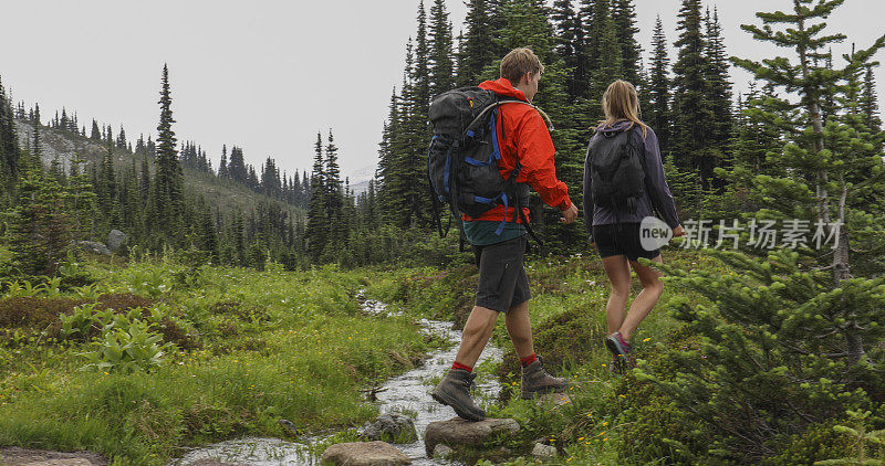 徒步旅行的夫妇沿着清澈溪流附近的林间小径散步