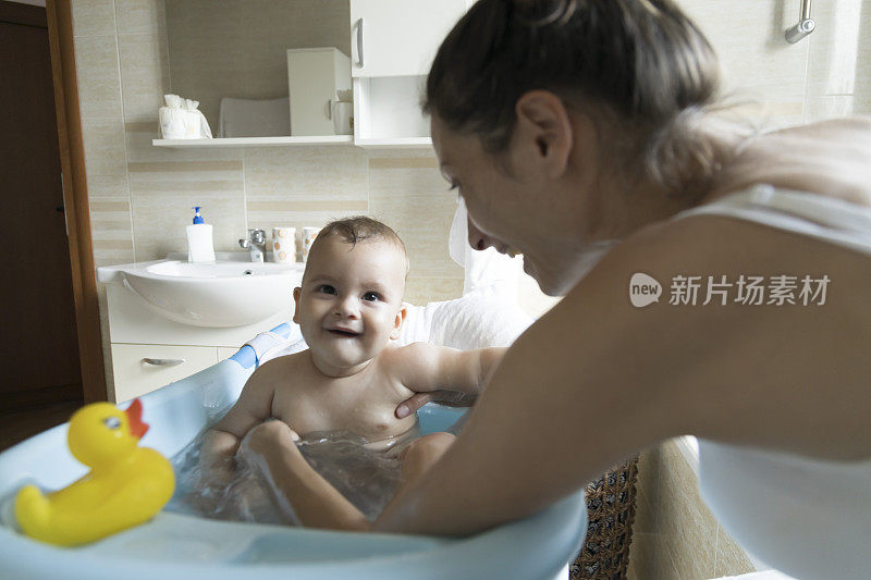 一位母亲在家里的浴室里给她的婴儿洗澡。用黄色的鸭子给婴儿洗澡很有趣。妈妈和她的孩子在洗澡