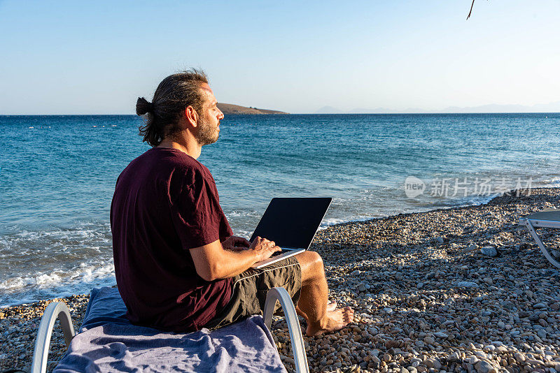 年轻的商人在海边用笔记本电脑工作