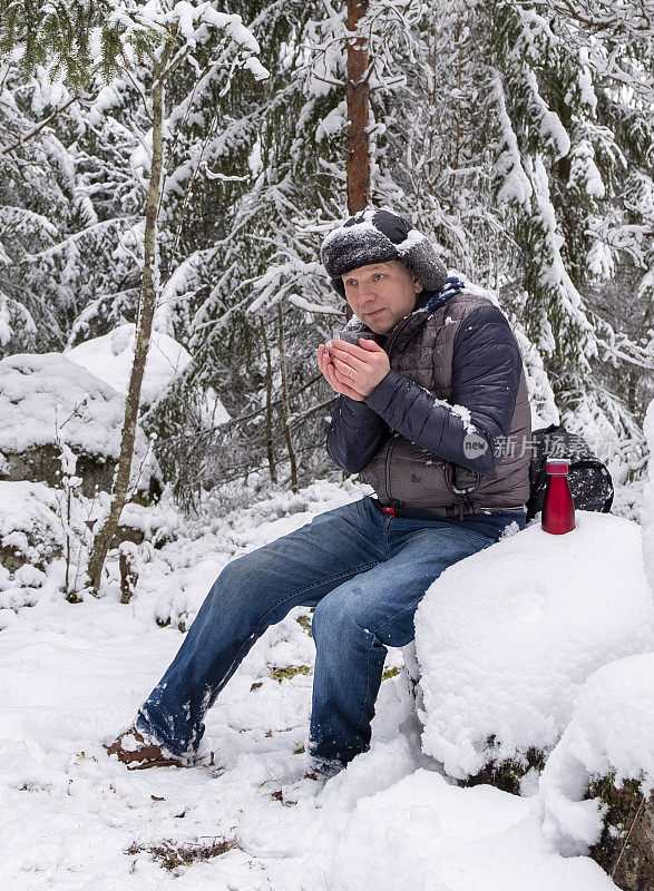 一个男人，一个白种人，正在冰天雪地的森林里喝热咖啡。