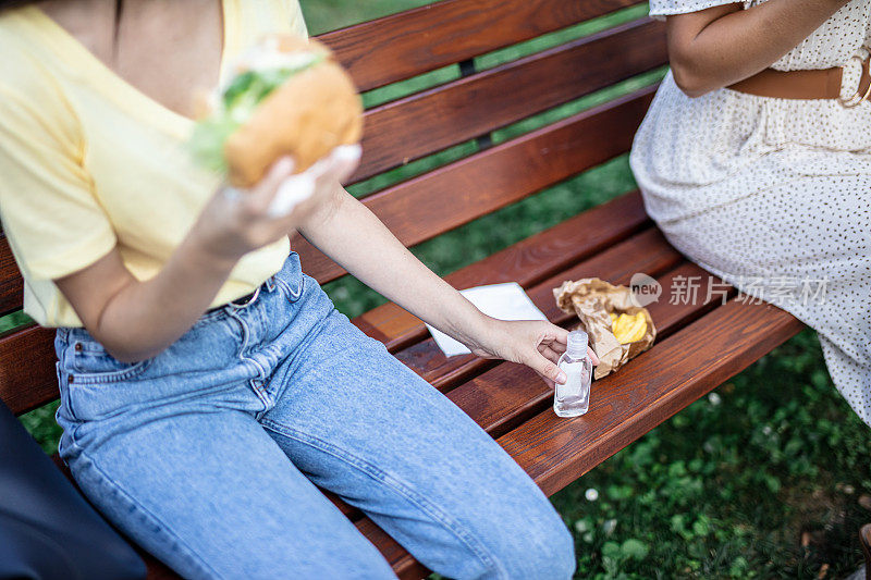 一名妇女在公园长凳上伸手去拿洗手液