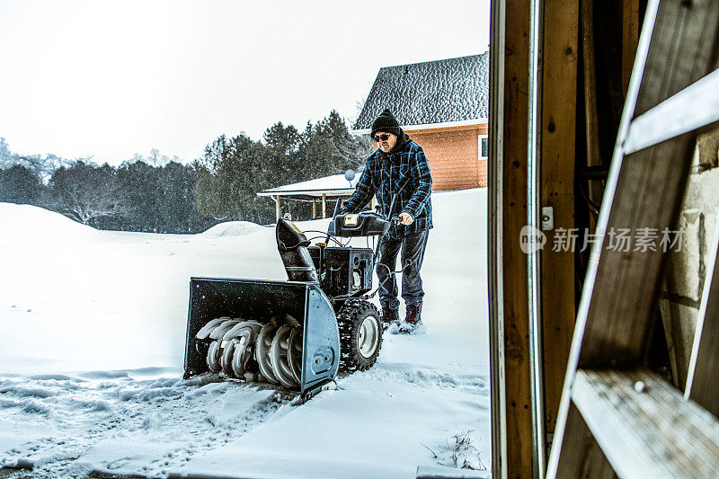 老人正在用吹雪机清理积雪。