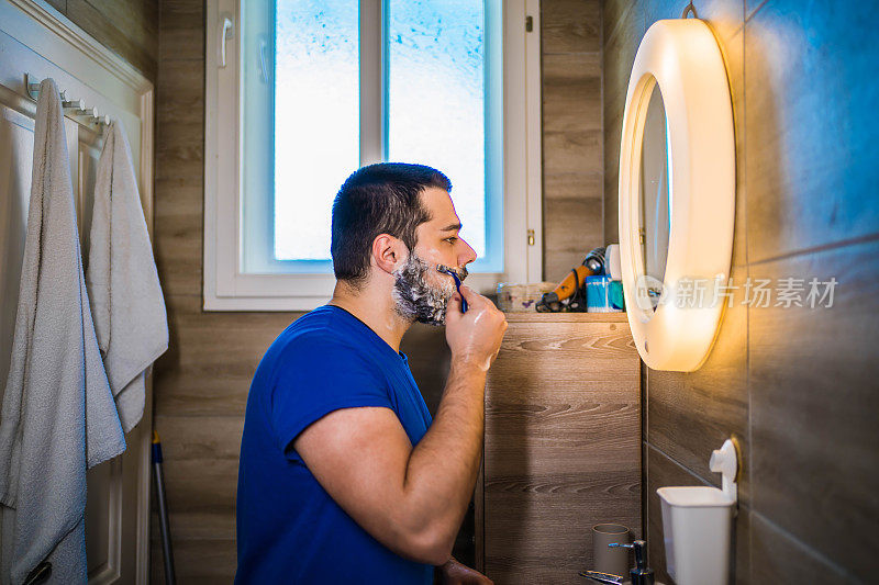 男人对着浴室的镜子刮胡子