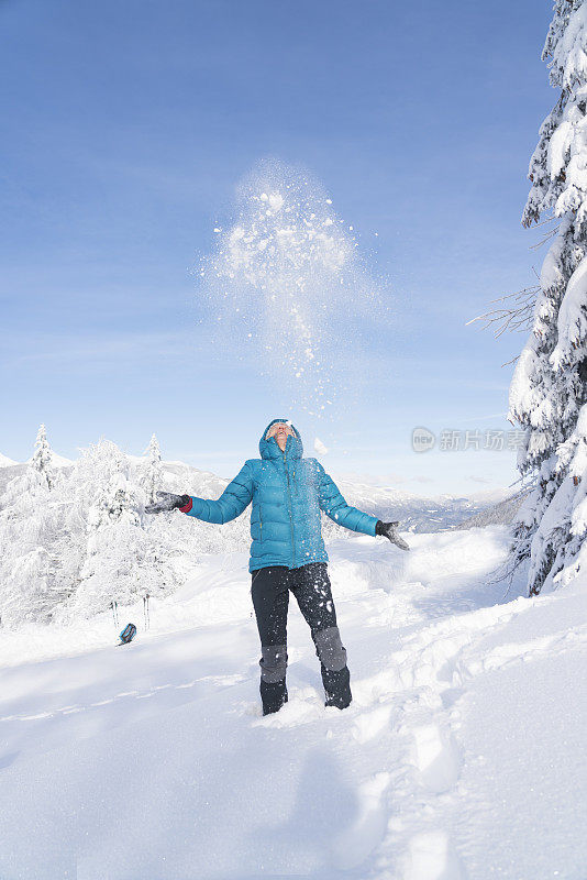 在冬天的森林里，成熟的女人穿着皮大衣向空中抛雪