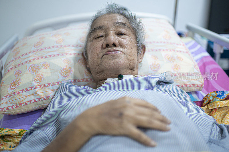 视频通话的亚洲华人老年人与气管切开管躺在床上看着摄像机
