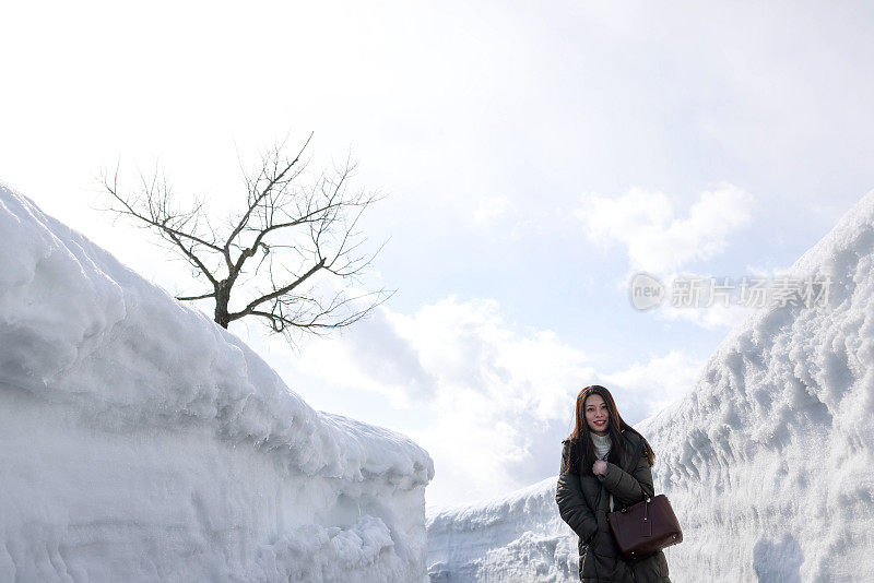 美丽的年轻女子走在雪堆之间的小路上