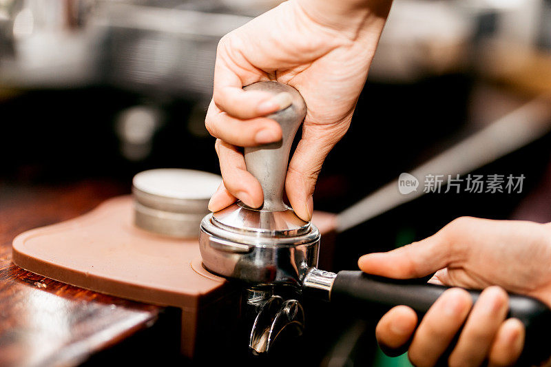 咖啡师使用浓缩咖啡捣固器将咖啡粉末压入咖啡过滤器中