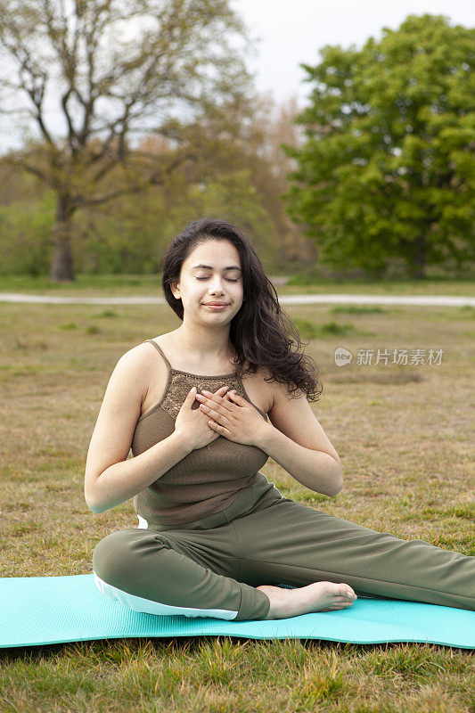 一名年轻女子在公园里做瑜伽，坐在绿松石色的运动垫上