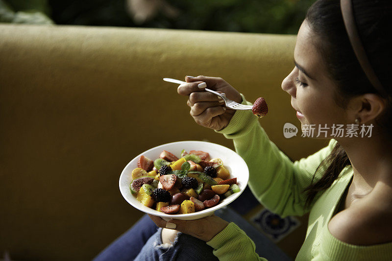 特写的一个西班牙可爱的年轻女人吃水果沙拉在户外午餐