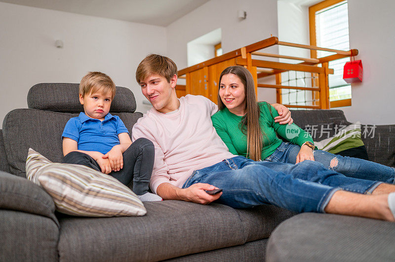 年轻的一家人坐在沙发上看电视
