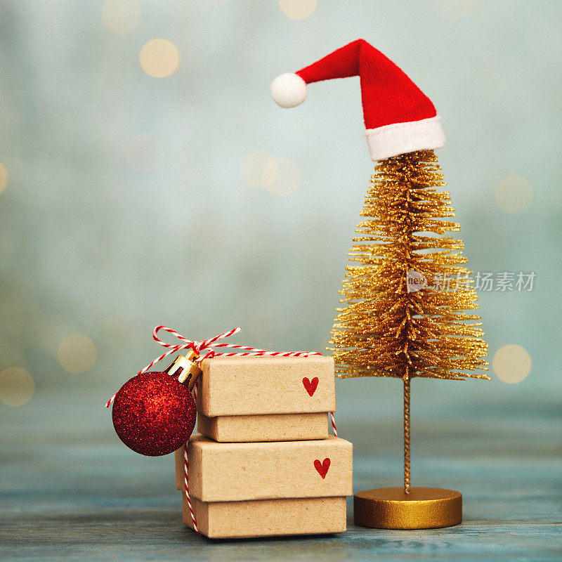 可爱的圣诞背景与堆叠的礼物和金色圣诞树戴圣诞帽。蓝色背景与串灯和复制空间