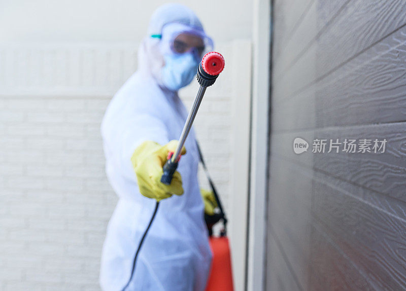 一名身穿防护服的男子正在用化学喷雾器消毒一栋建筑