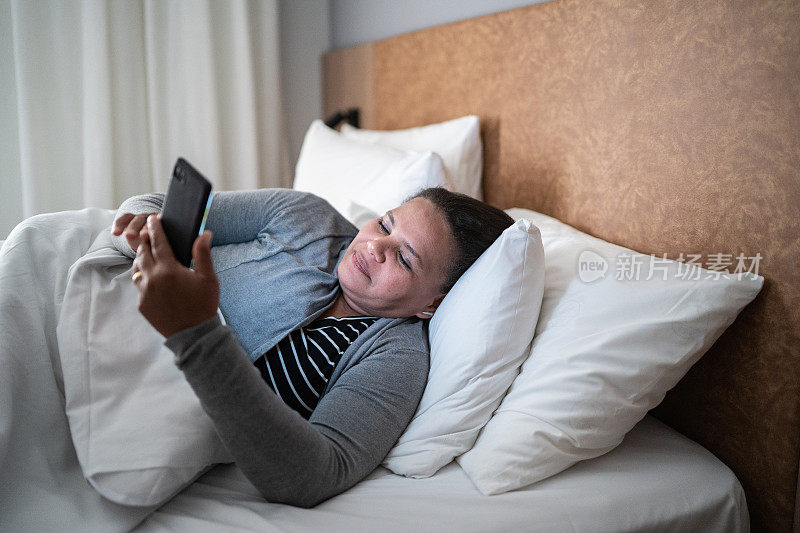一个成熟的女人躺在床上玩手机