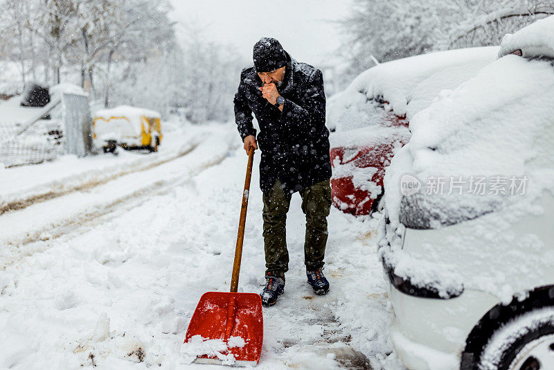 拿着雪铲的成熟男人。积雪下的汽车和街道。