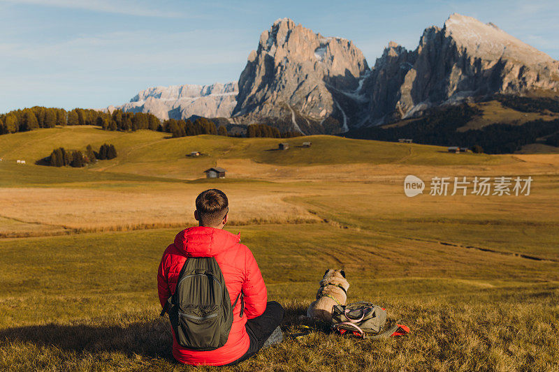 男性旅行者和他的狗在阿尔卑斯山的白云石山脉凝视日落的后视图