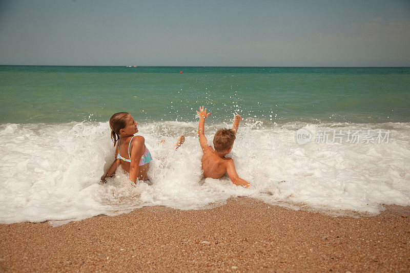 一个晴朗的夏日，一女一男两个孩子在浪花飞溅的海水中嬉戏