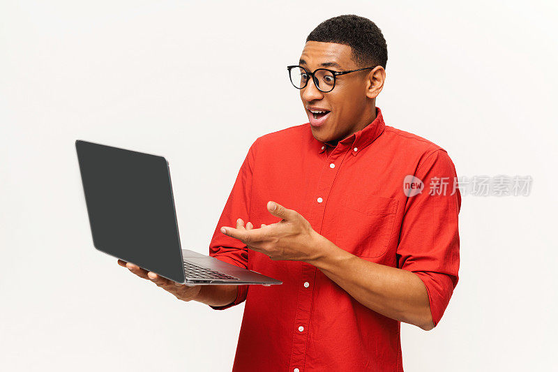 英俊的非洲裔美国男性企业家穿着休闲的红色衬衫，戴着时髦的眼镜，看着笔记本电脑屏幕