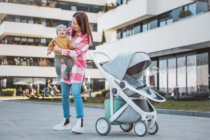 年轻的妈妈抱着婴儿，推着现代的婴儿车，漫步在城市中