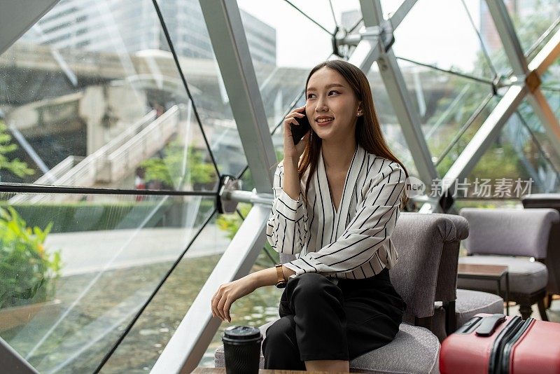 美丽的年轻亚洲女性商务独自女旅行者在机场候机楼的咖啡馆里等待起飞时用智能手机打电话