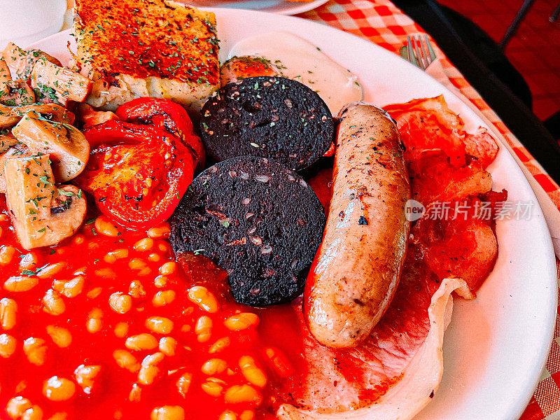 一顿传统英式早餐的特写镜头，包括坎伯兰式香肠、煎蛋、泡泡和Squeak、培根、烤豆、黑布丁、蘑菇和烤番茄