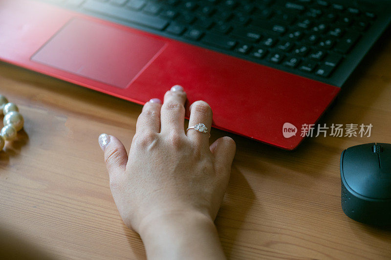 女人在木制办公桌上使用笔记本电脑工作时，手上会拿着钻石戒指等奢侈品。