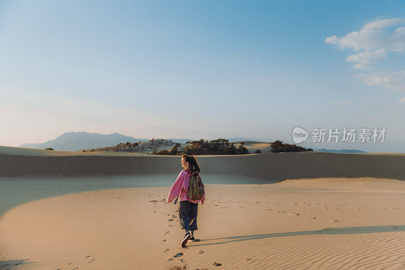 在土耳其海边的沙丘上，背着背包的女人凝视着风景优美的日落